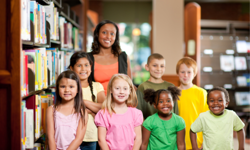 Several smiling children standing in a library.